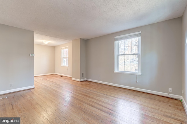 spare room with light wood finished floors, a textured ceiling, and baseboards