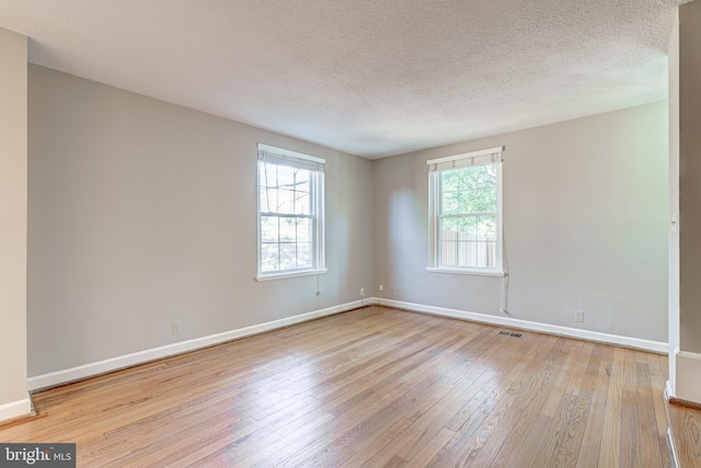 spare room featuring visible vents, baseboards, a textured ceiling, and hardwood / wood-style flooring