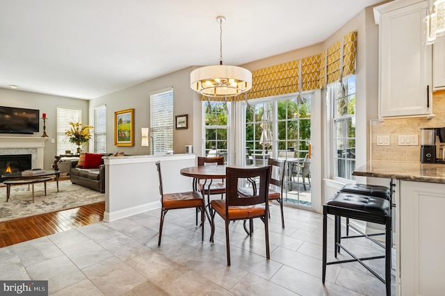 dining room with light tile patterned floors, a glass covered fireplace, baseboards, and an inviting chandelier