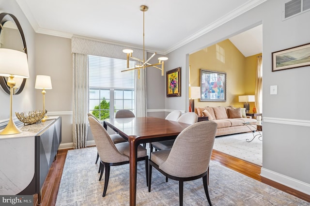 dining room with a notable chandelier, ornamental molding, visible vents, and wood finished floors