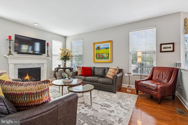 living room featuring visible vents, wood-type flooring, a lit fireplace, and baseboards