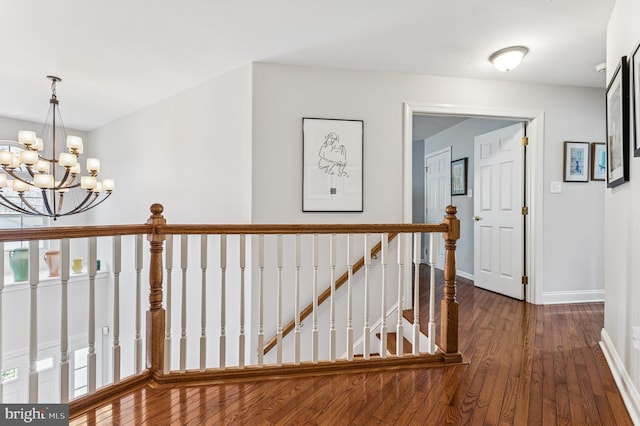 hall with an upstairs landing, baseboards, an inviting chandelier, and dark wood finished floors