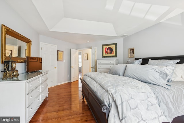 bedroom with baseboards, a tray ceiling, and wood finished floors