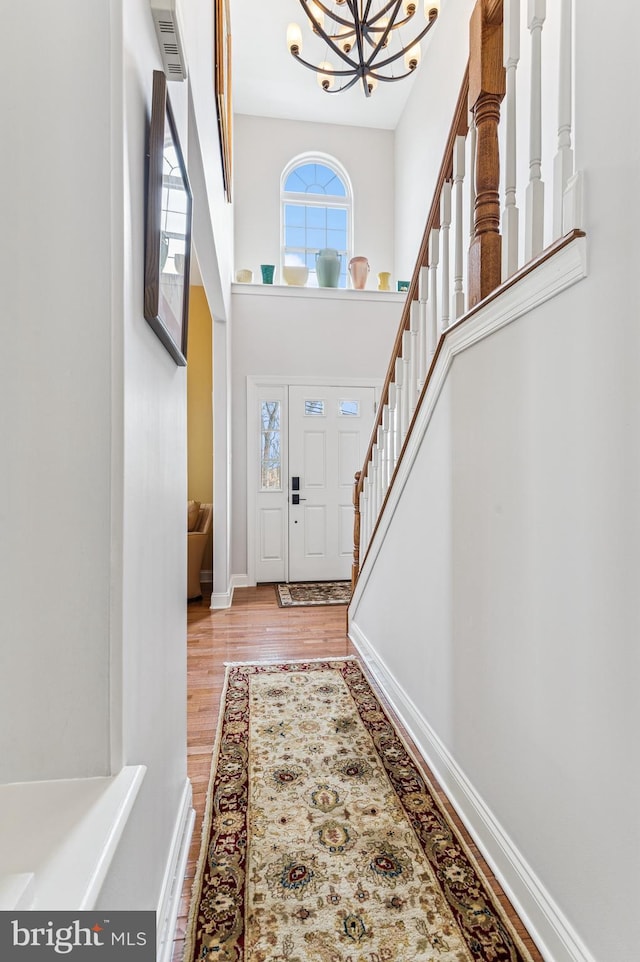 foyer featuring baseboards, an inviting chandelier, wood finished floors, and a towering ceiling