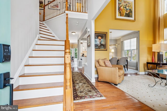 stairway featuring baseboards, wood-type flooring, a high ceiling, and ornamental molding