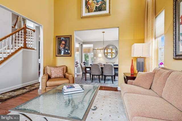 living area featuring wood finished floors, baseboards, an inviting chandelier, a high ceiling, and stairs