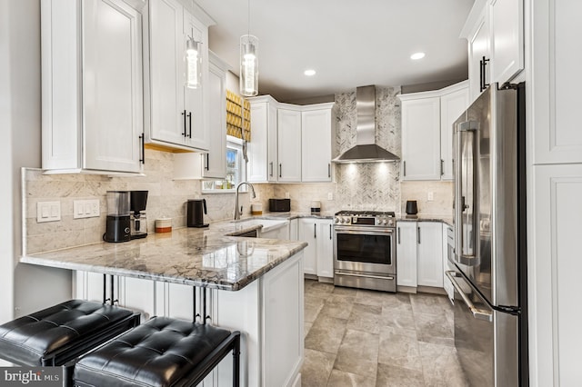 kitchen with light stone counters, a peninsula, appliances with stainless steel finishes, white cabinetry, and wall chimney exhaust hood