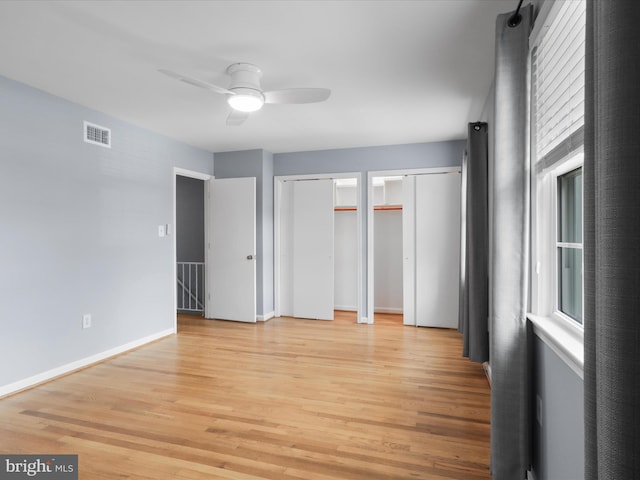 unfurnished bedroom with multiple windows, visible vents, light wood finished floors, and multiple closets