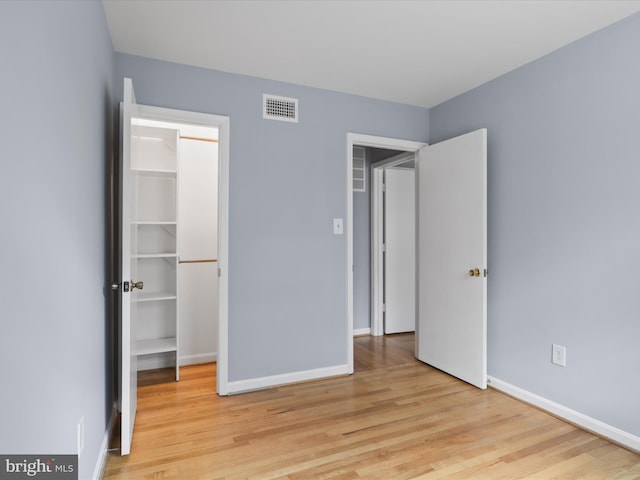 unfurnished bedroom featuring baseboards, visible vents, a closet, a walk in closet, and light wood-type flooring