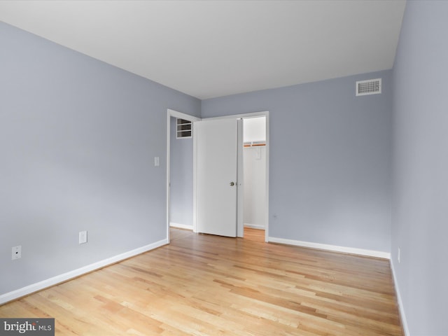 unfurnished bedroom featuring wood finished floors, visible vents, baseboards, a closet, and a walk in closet