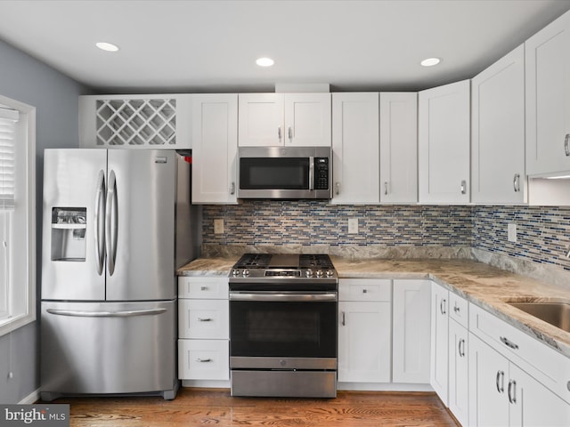 kitchen featuring light wood finished floors, decorative backsplash, recessed lighting, white cabinets, and stainless steel appliances