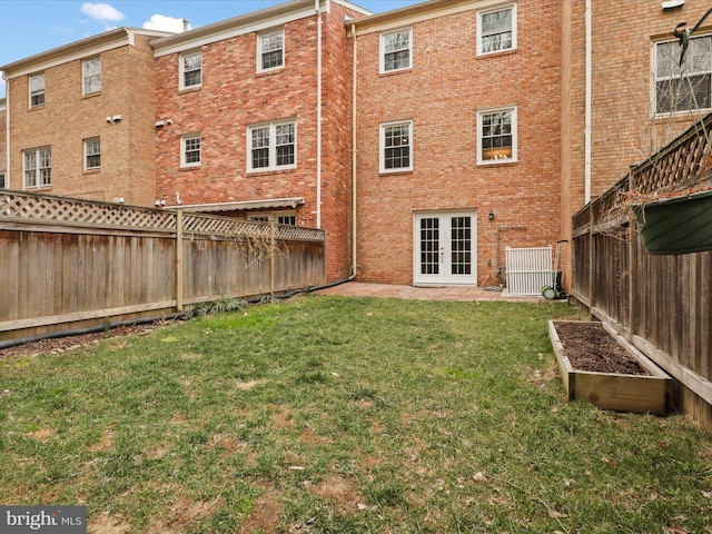 rear view of house featuring french doors, a lawn, a fenced backyard, and brick siding