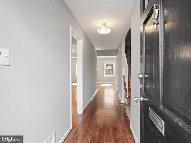 corridor with stairway, visible vents, baseboards, and dark wood-style flooring