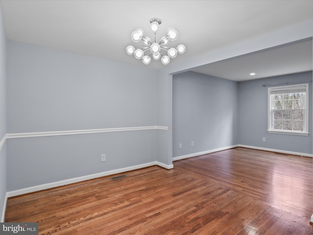 unfurnished room featuring a chandelier, visible vents, baseboards, and wood finished floors