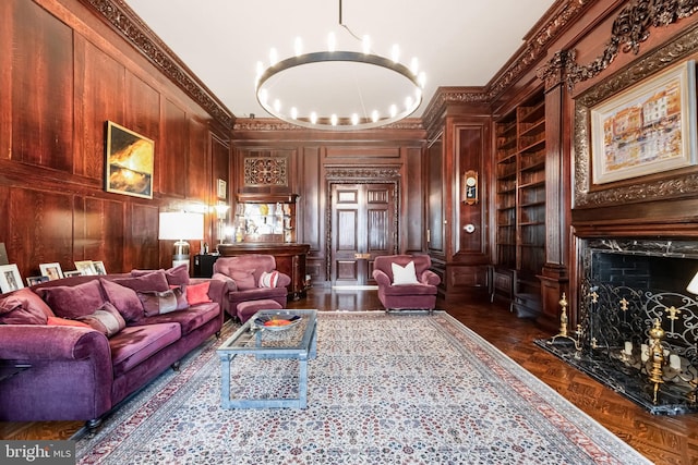 living area with wooden walls, crown molding, built in features, a fireplace, and an inviting chandelier