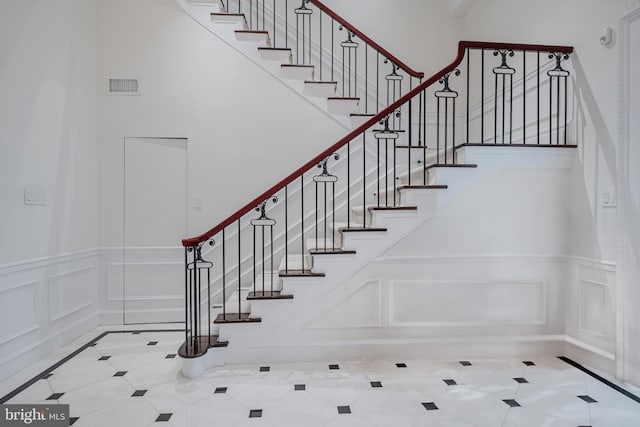 stairs with visible vents, a towering ceiling, and a decorative wall