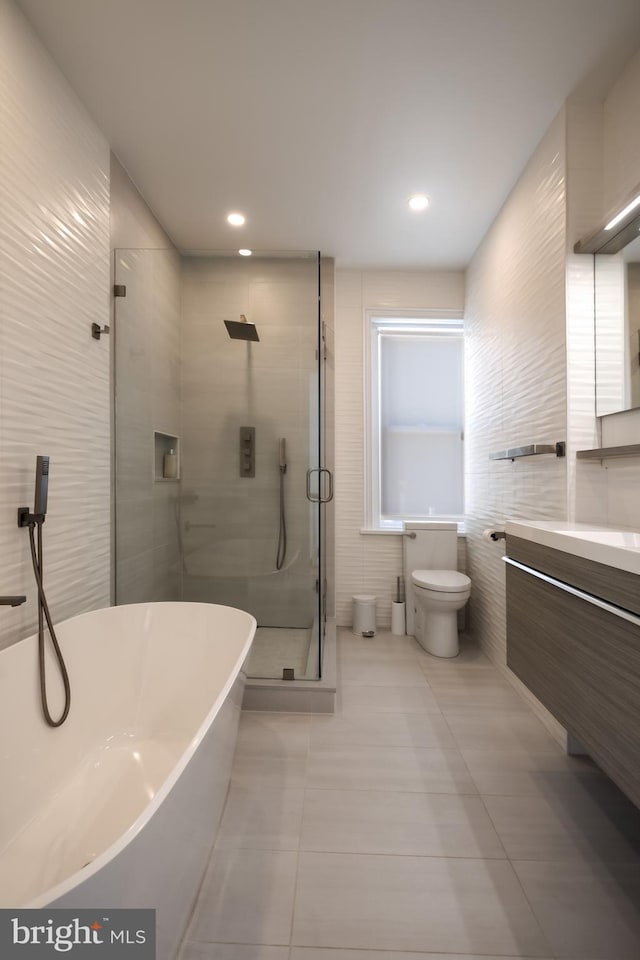 full bathroom featuring a freestanding tub, toilet, a stall shower, tile walls, and vanity