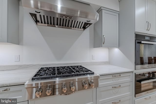 kitchen featuring ventilation hood, light stone countertops, white cabinetry, and stainless steel gas cooktop