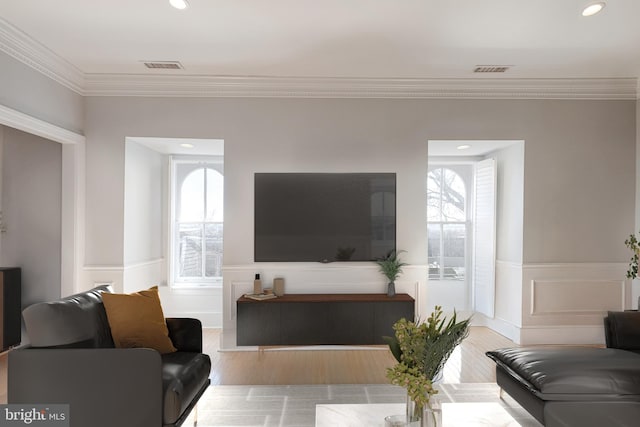 living room with a wealth of natural light, visible vents, crown molding, and a wainscoted wall