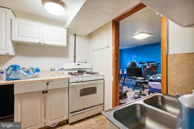 kitchen with light tile patterned floors, white range with gas cooktop, a sink, light countertops, and white cabinets