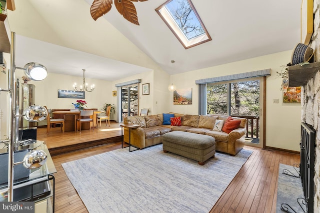 living room with ceiling fan with notable chandelier, a fireplace, baseboards, and wood-type flooring