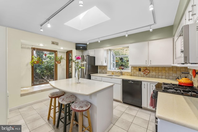 kitchen featuring light countertops, decorative backsplash, a skylight, white cabinets, and stainless steel appliances