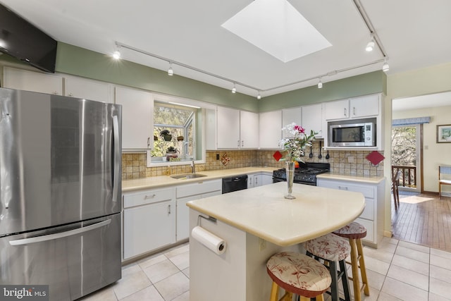 kitchen featuring light countertops, a skylight, white cabinets, black appliances, and a sink