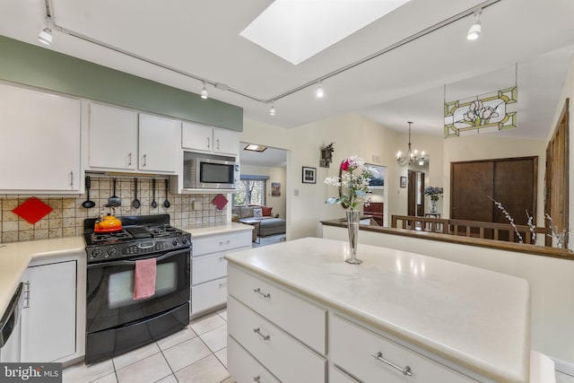 kitchen with a skylight, light countertops, black gas range, stainless steel microwave, and backsplash