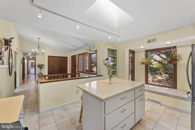 kitchen featuring visible vents, lofted ceiling with skylight, a kitchen island, white cabinetry, and light tile patterned floors