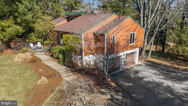 view of side of property with driveway, an attached garage, and a shingled roof