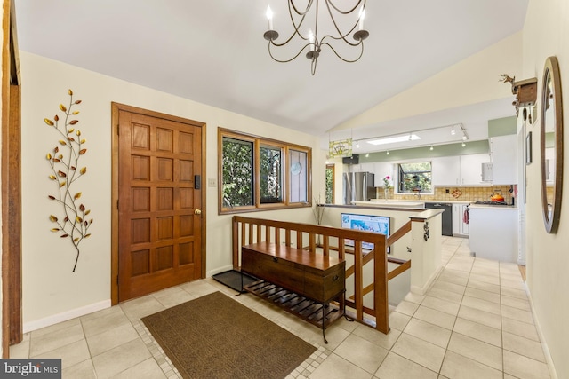 entryway with light tile patterned floors, baseboards, a notable chandelier, and vaulted ceiling