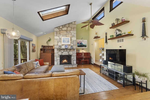 living area with visible vents, ceiling fan, a fireplace, a skylight, and wood-type flooring