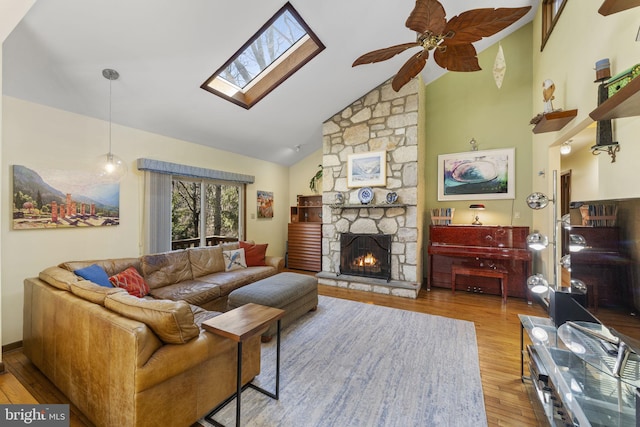 living room featuring ceiling fan, a stone fireplace, a skylight, wood finished floors, and high vaulted ceiling