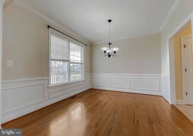 unfurnished dining area with wainscoting, ornamental molding, a chandelier, and light wood-style floors