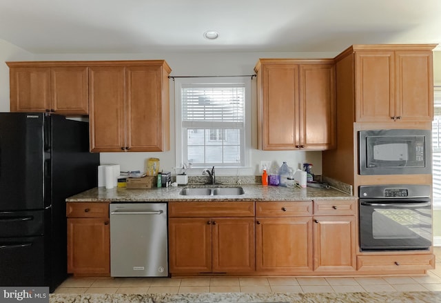 kitchen featuring a sink, brown cabinetry, black appliances, light tile patterned flooring, and light stone countertops