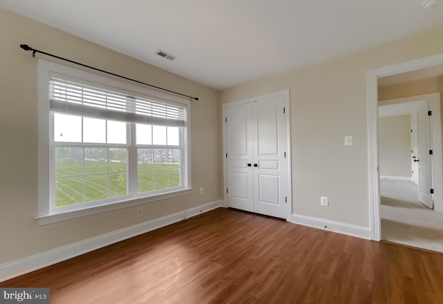 unfurnished bedroom with a closet, wood finished floors, visible vents, and baseboards