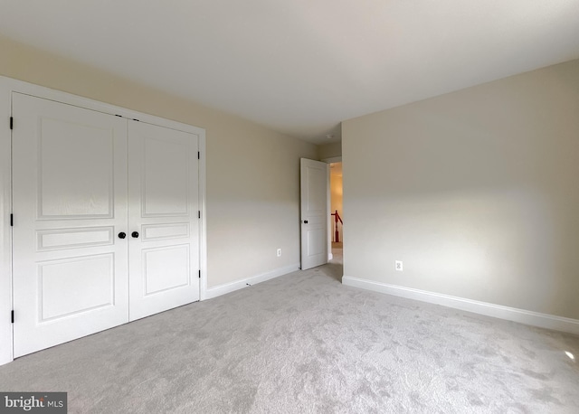 unfurnished bedroom featuring baseboards, a closet, and light colored carpet