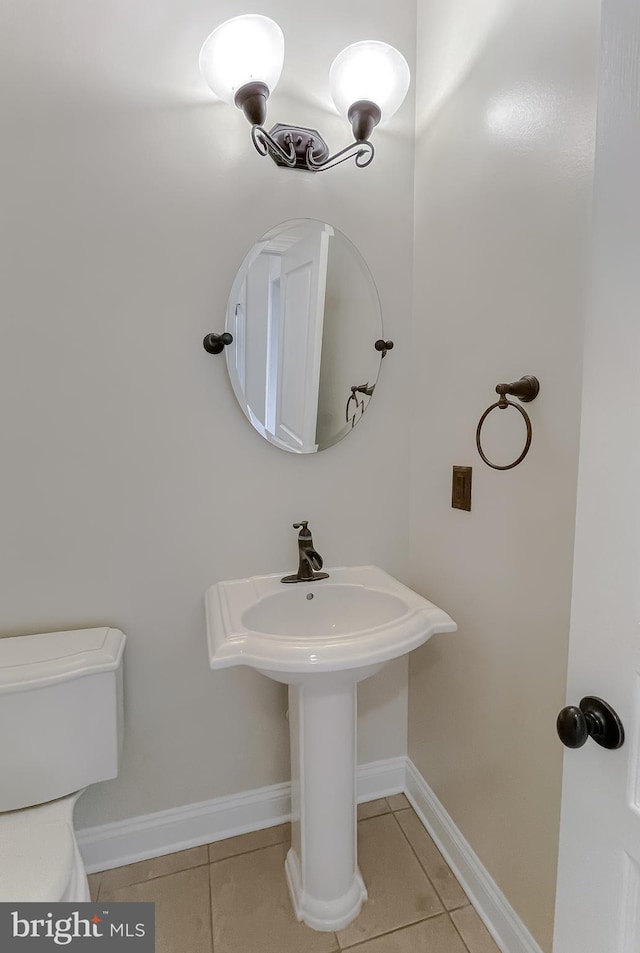 half bath with tile patterned floors, baseboards, a sink, and toilet