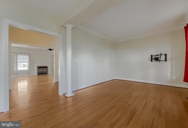 empty room featuring light wood finished floors, crown molding, baseboards, decorative columns, and a fireplace
