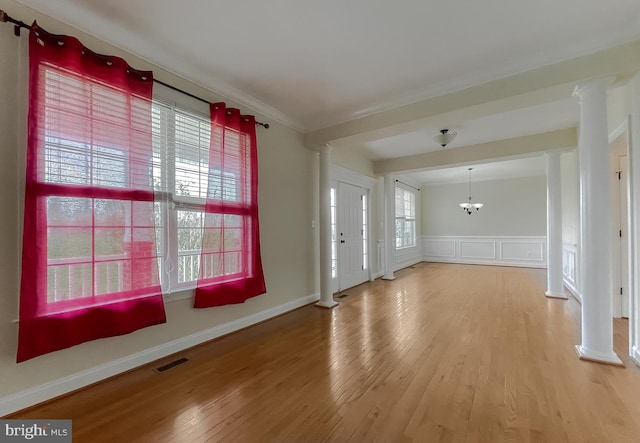 unfurnished living room with wood finished floors, a chandelier, ornamental molding, visible vents, and ornate columns