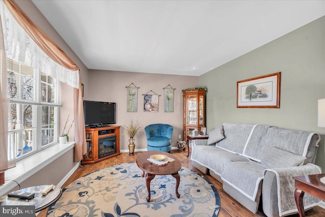 living area with a glass covered fireplace, light wood-style floors, and baseboards