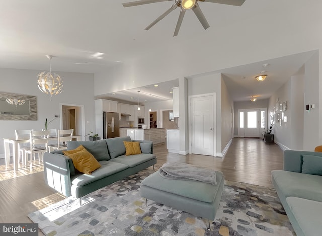 living area featuring ceiling fan with notable chandelier, baseboards, light wood-type flooring, and high vaulted ceiling