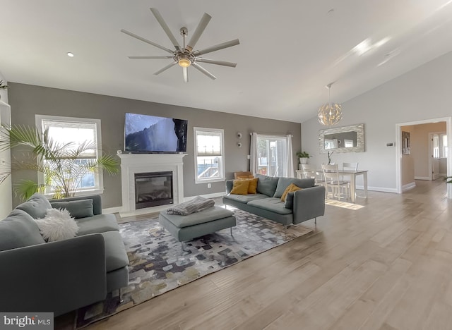 living area featuring a glass covered fireplace, high vaulted ceiling, baseboards, and wood finished floors