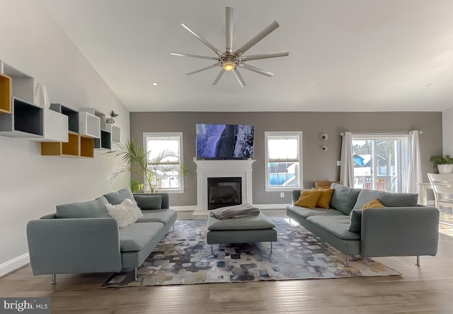 living area with a glass covered fireplace, lofted ceiling, wood finished floors, and baseboards