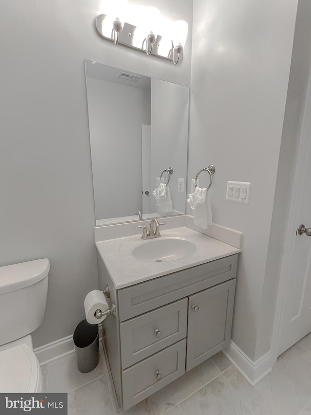 half bath with vanity, toilet, baseboards, and marble finish floor