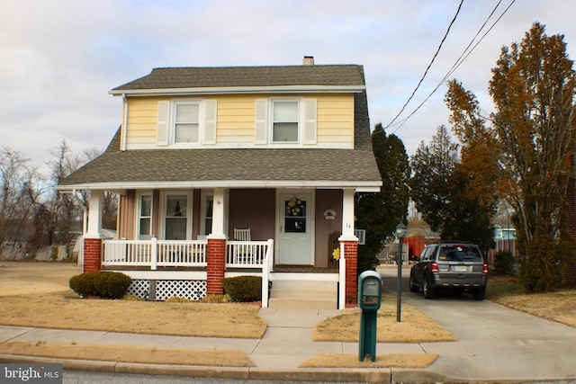 view of front facade with a porch, concrete driveway, a chimney, and a shingled roof