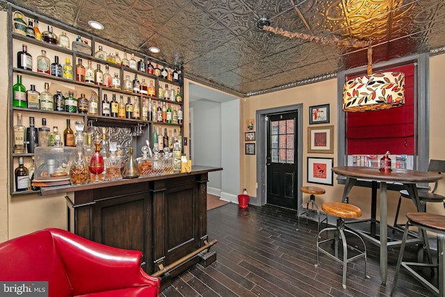 bar featuring an ornate ceiling, a bar, baseboards, and dark wood-style flooring