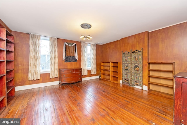 interior space with baseboards, a notable chandelier, hardwood / wood-style floors, and wooden walls