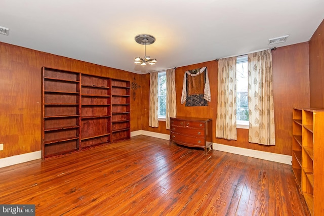 spare room with visible vents, wood-type flooring, wooden walls, and an inviting chandelier