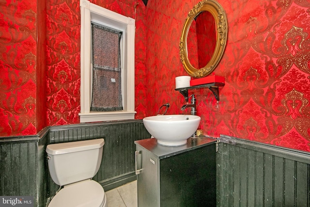 bathroom featuring tile patterned floors, toilet, wainscoting, wallpapered walls, and vanity